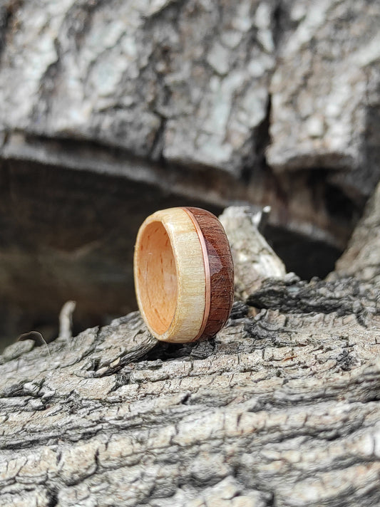 Handmade wooden ring made of beech, birch, and walnut veneer with a copper wire accent, displayed on tree bark.